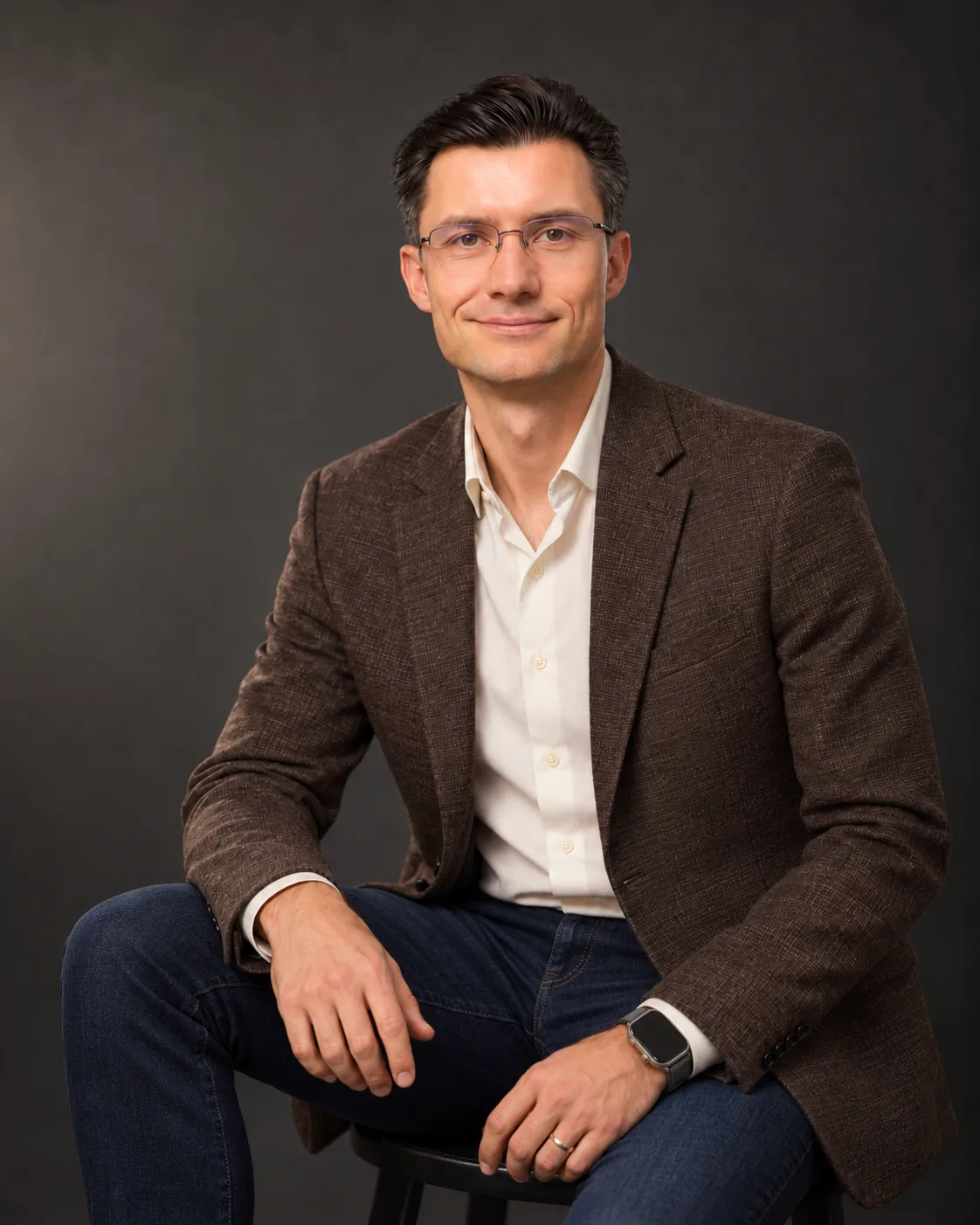 Mihai Nadăș seated in an espresso jacket, ivory shirt and dark-indigo jeans.